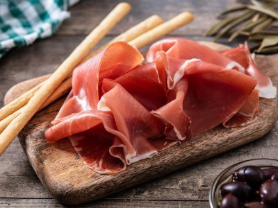 Spanish serrano ham with olives and breadstick on wooden table background